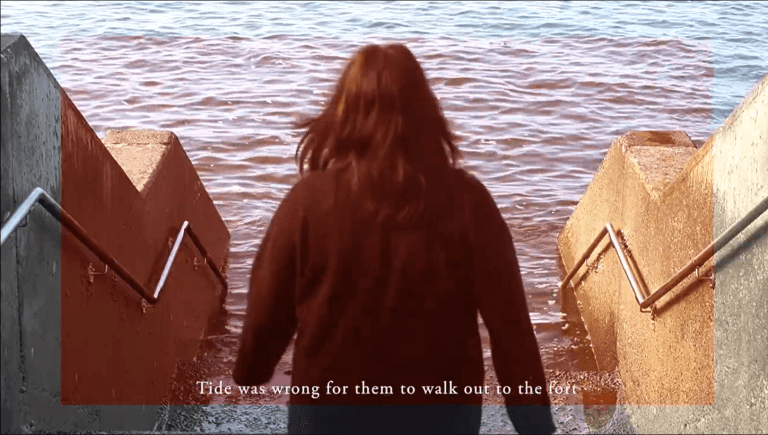 FIlm still showing a person in a black dress walking down steps into the sea
